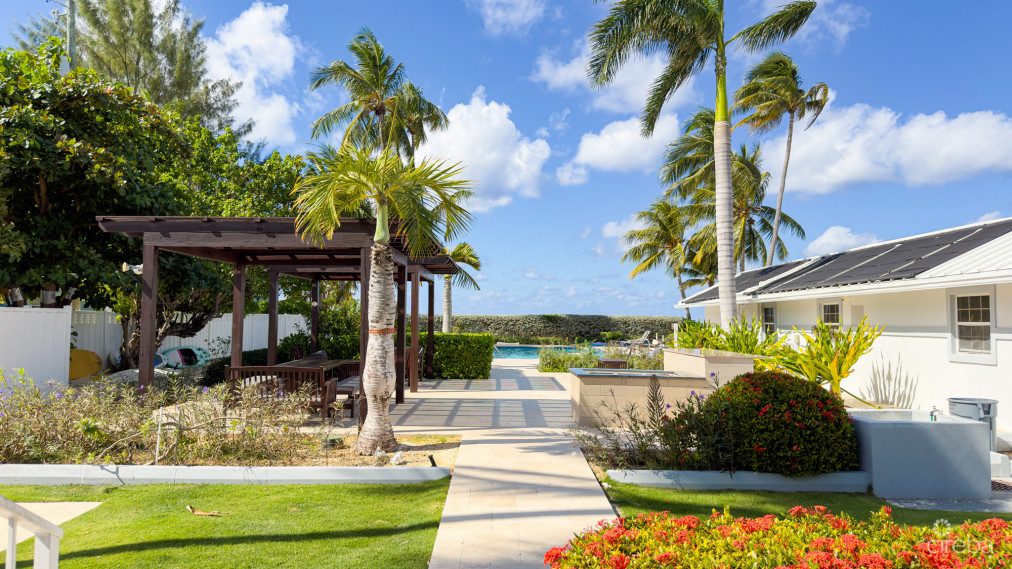 Landscaped grounds and shaded pool pergola at Island Pine Villas, with palms and the villas beyond
